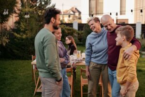 Happy family in casual clothes laughing and having picnic in backyard with string of light bulbs in daytime